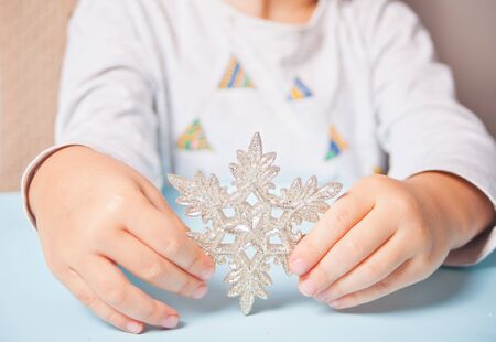 Girl's hand holding a Christmas decor big snowflake in a hands on the blue background.の写真素材