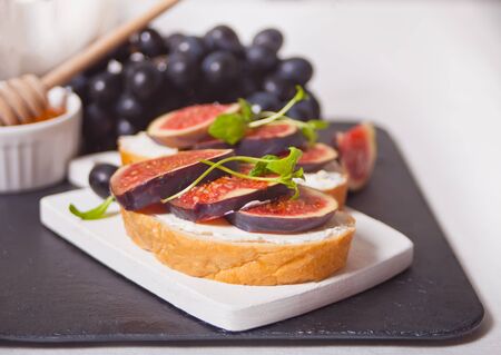 Sandwich with cream cheese, figs and honey served on a small white cutting board. Healthy food concept.の写真素材