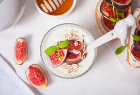 Yogurt with muesli and fig fruit, sandwich with cream cheese, figs and honey on the white background. Healthy food concept. Top view.の写真素材