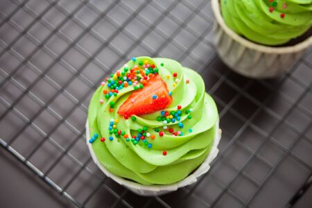Close up cupcakes with green icing and strawberry on a metal baking rack. Top view.の写真素材