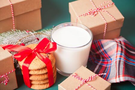 Glass of milk, cookies, Christmas gift boxes and pine branch on the green table.の写真素材