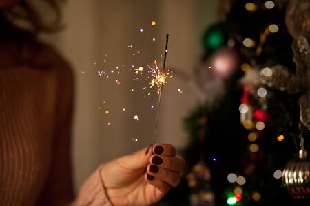 Glowing sparkler in pretty woman hand in dark festive room. Merry Christmas and Happy New year