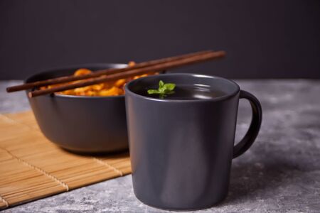 Udon noodles with chicken meat in bowl with chopsticks and cup of tea on dark stone background.の写真素材