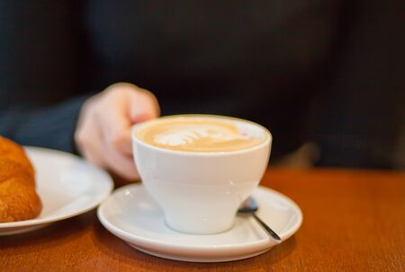 Woman hand holding white cup of cappuccino.の写真素材