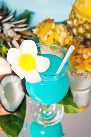 Exotic tropical Blue Curacao cocktail drink in a glass with Plumeria frangipani flower, palm leaf, fresh coconut, friut salad on the backgroundの写真素材