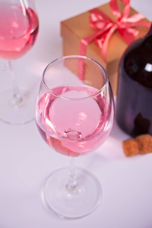 Two glasses with pink grape wine with flowers, bottle and gift box on the background. Romantic dinner conceptの写真素材