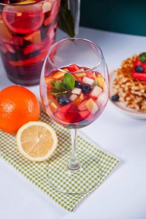 Red wine fresh sangria or punch with fruits, mint leaves and berries. Homemade waffles on the backgroundの写真素材
