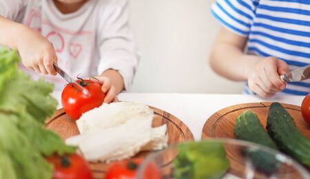 Happy children prepares vegetables for salad in home kitchen. Healthy eatingの写真素材