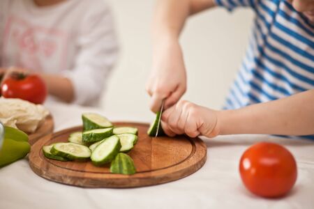 Happy children prepares vegetables for salad in home kitchen. Healthy eatingの写真素材