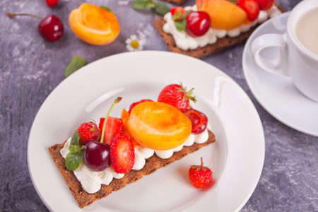 Crisp fitness health bread with creme cheese, fruit and berries and cup of tea on the white plate on the white wooden backgroundの写真素材