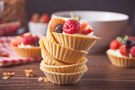 Delicious mini tart tartlets with fresh berries on wooden background.