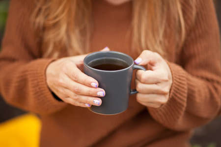 Outdoors autumn picnic. Young woman holding mug of hot coffee in a hand.の写真素材