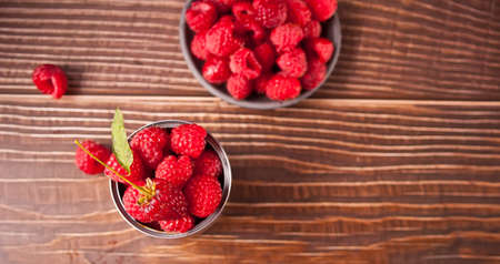 Fresh ripe organic raspberry in tin can and plate on rustic wooden table