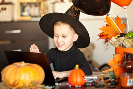 funny kid boy in witch costume for Halloween using a digital tablet laptop notebook. Online call friends or parentsの写真素材