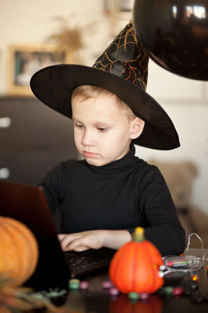funny kid boy in evil costume for Halloween using a digital tablet laptop notebook. Online call friends or parents.の写真素材