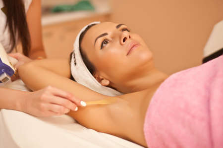 Beautician waxing female armpits in spa center