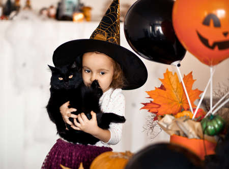 funny child girl in witch costume for Halloween with black cat in a hands.の写真素材