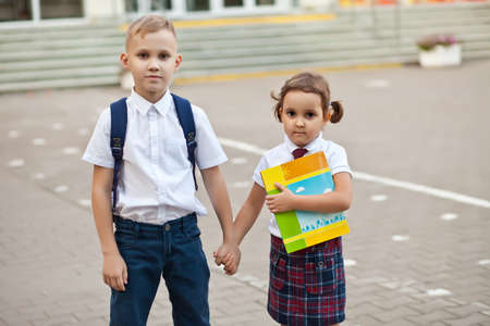 Kids schoolboy and schoolgirl in uniform standing near by school and holding a handsの写真素材
