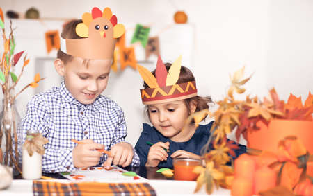 Girl and boy in paper turkey and native American hats writing I am thankful for. Celebrating Thanksgiving day. Diy craft art project.の写真素材