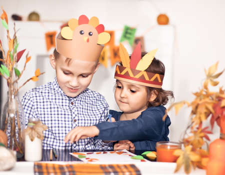 Girl and boy in paper turkey and native American hats writing I am thankful for. Celebrating Thanksgiving day. Diy craft art project.の写真素材