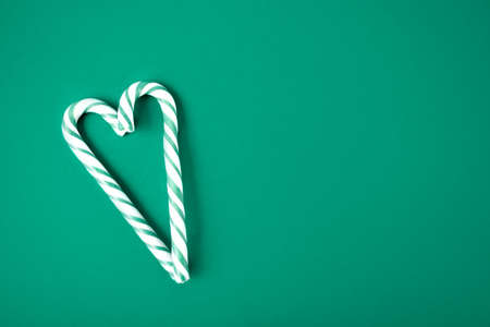 Green and white candy cane in the shape of heart on the green backgroundの写真素材