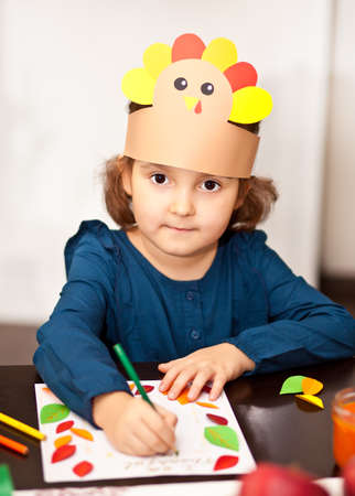 Little cute girl in paper turkey hat writing I am thankful for. Celebrating Thanksgiving day. Diy craft art project.の写真素材