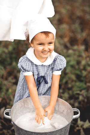 Baby girl washing clothes by hand in a tin basin. Retro style. Hand washing.の写真素材