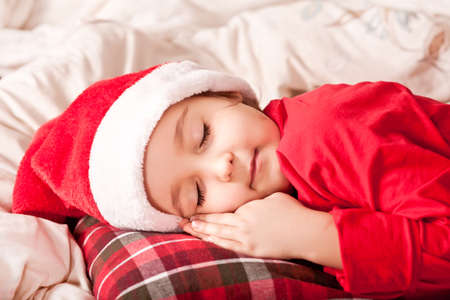 happy child girl in Santa cap waiting Santa and sleep near pine tree on Christmas eveの写真素材