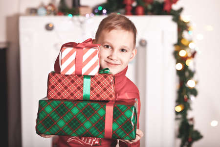 Child boy kid in red knitted sweater holding a Christmas gift boxes in a handsの写真素材