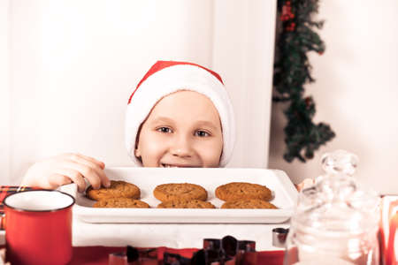 Kid boy in Santa cap taking try to steal cookie from table.の写真素材