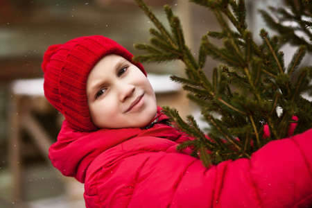 Smiling kid boy in winter clothes holding christmas tree in outdoor shop market. Christmas, New Year concept.の写真素材