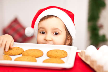 Kid girl in Santa cap taking try to steal cookie from table.の写真素材
