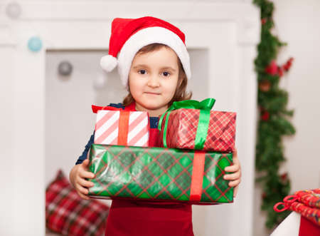 Child little cute girl kid in Santa cap holding a Christmas gift boxes in a handsの写真素材