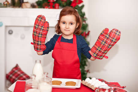 Little cute girl in red apron baking Christmas cookies at homeの写真素材
