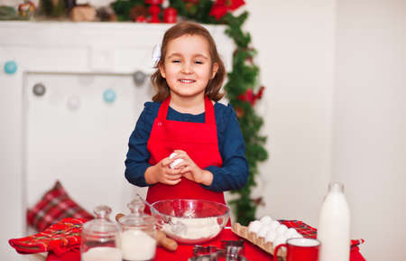 Little cute girl in red apron baking Christmas cookies at homeの写真素材