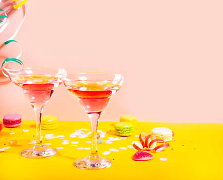 Glasses of pink cocktails with heart candies on yellow table. Birthday party or Valentines day...