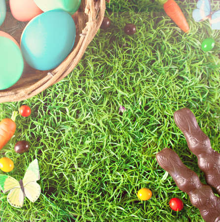 Easter colorful eggs, chocolate bunny, carrots candy in the grass. Top view. Copy space.