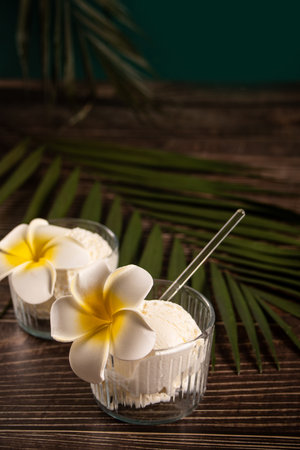 Delicious tropical flavors ice cream sorbet sundae decorated with flower plumeria frangipani and palm leaf on the background . summer food conceptの写真素材