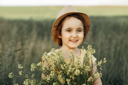 Little toddler girl in a yellow dress walking and picking yellow flowers on a meadow field.