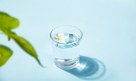 Fresh clear water drink with white flower apple tree in glass on blue backgroundの写真素材