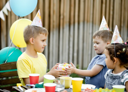 Cute funny nine year old boy celebrating his birthday with family or friends with homemade baked cake in a backyard. birthday party for kids. His gets presents gift box and enjoy the surprise .の写真素材