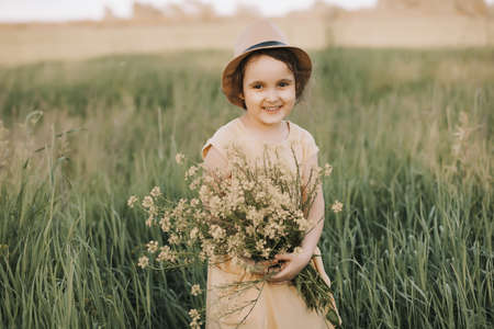Little toddler girl in a yellow dress walking and picking yellow flowers on a meadow field.の写真素材