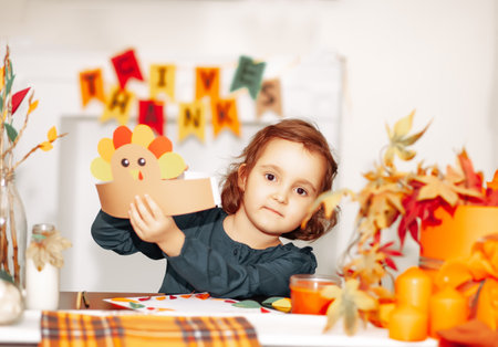 Little cute girl made paper turkey hat for celebrating Thanksgiving day. DIY craft art projectの素材