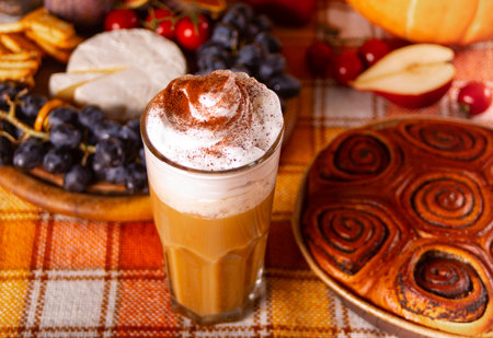 Pumpkin spice whipped latte in glass. Hot autumn beverage. Nearby delicious pie and appetizers fruits and cheeseの写真素材