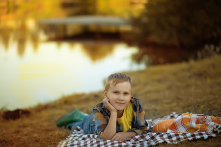 Thinking dreaming boy child lies on blanket near a river or lakeの写真素材