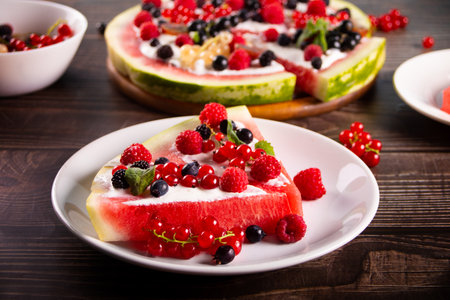 Colorful summer watermelon piece of cake with whipped cream and berries on wooden table. Refreshment summer dessert food.の写真素材