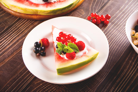 Colorful summer watermelon piece of cake with whipped cream and berries on wooden table. Refreshment summer dessert food.の写真素材