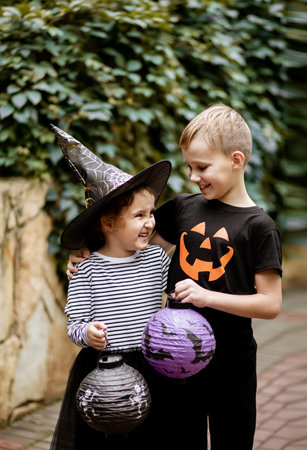 Little cute girl in witch costume and boy in jack-o-lantern t-shirt holding paper lanterns. Kids having fun on Halloween holiday.の写真素材