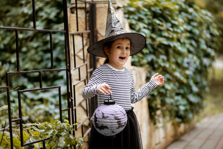 Little cute girl in witch costume holding paper lantern. Kid having fun on Halloween holidayの写真素材