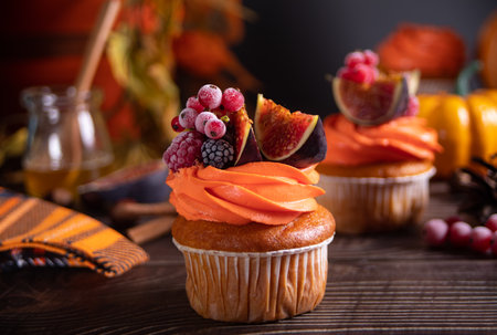 Delicious homemade autumn season spicy pumpkin cupcakes with whipped orange cream with fruit figs and frozen berriesの写真素材